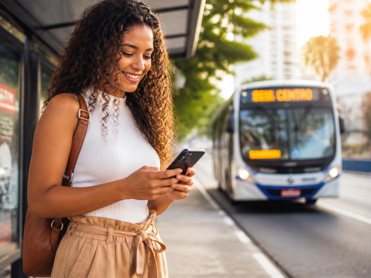 Passageira esperando o ônibus e acompanhando a chegada pelo celular
